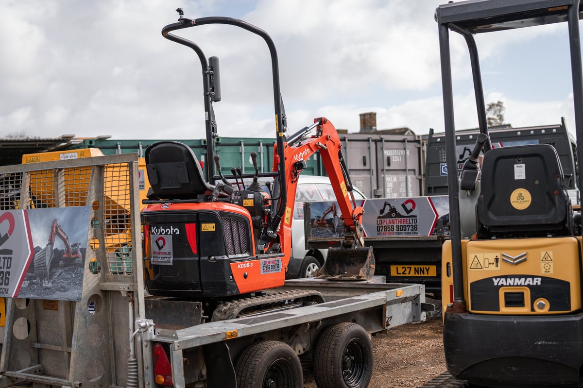 Orange Kubota mini excavator on a flatbed trailer with a yellow Yanmar excavator beside it