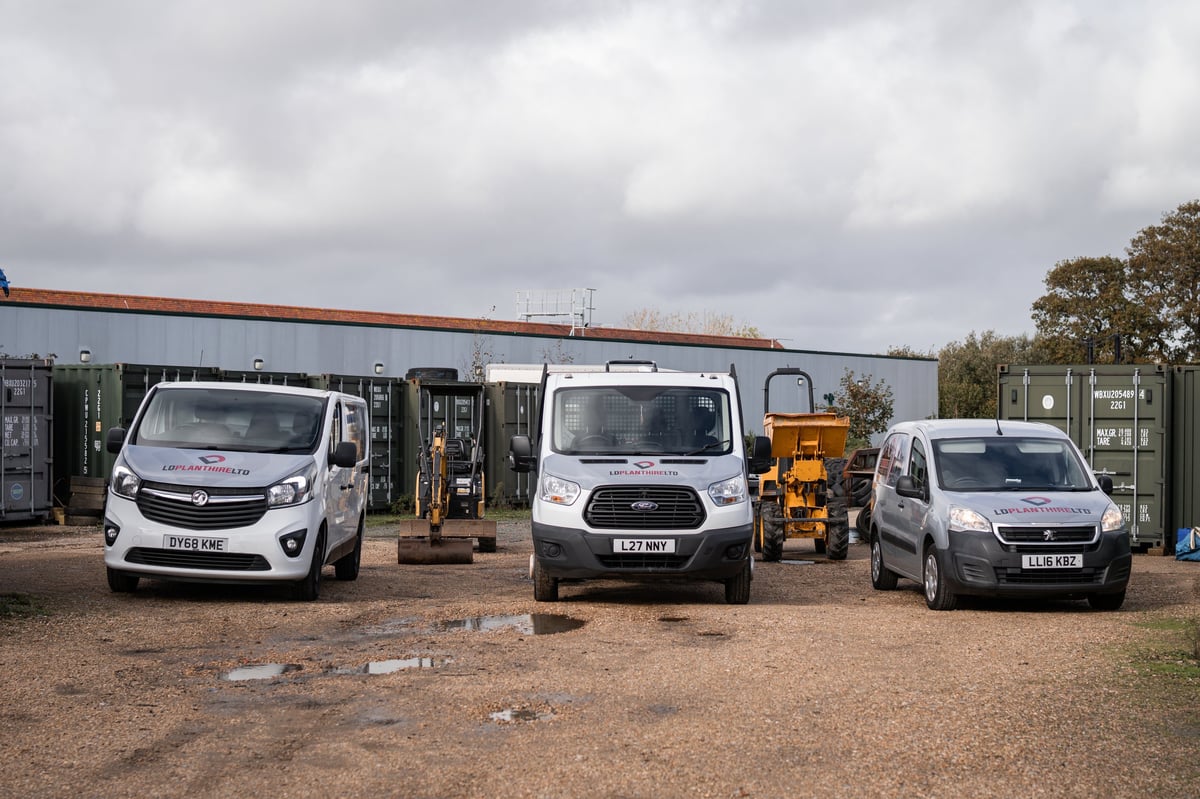Three LD Plant Hire vans parked outside the yard with shipping containers behind